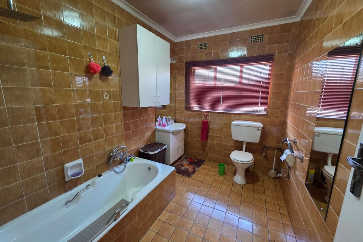 A functional bathroom featuring a bathtub with shower head, vanity cabinet, toilet, and full-height wall tiling.