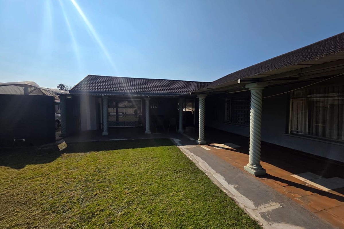 A spacious rear exterior view featuring a covered patio with decorative columns, overlooking a well-maintained lawn area.