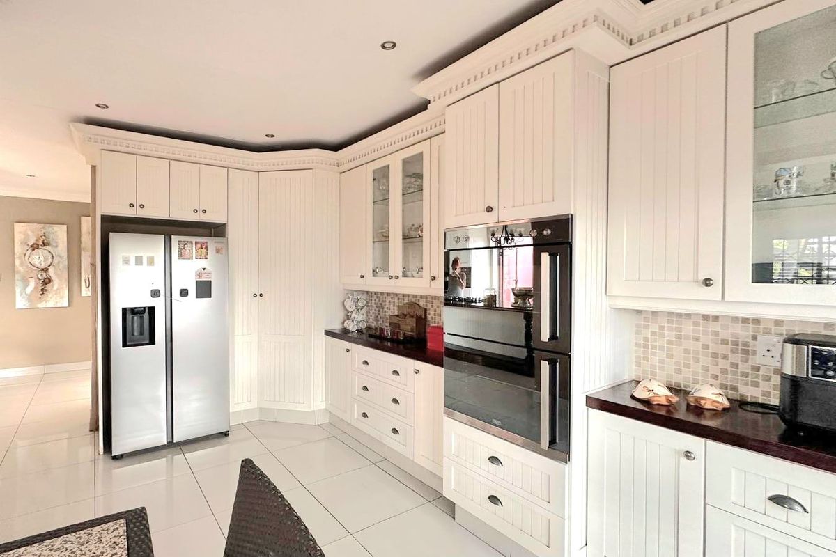 A well-maintained kitchen featuring white cabinetry, a double wall oven, mosaic tile backsplash, and polished floor tiles.