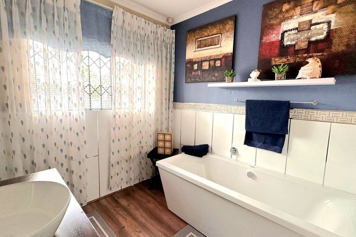 A well-maintained bathroom featuring a modern freestanding bathtub, a vessel sink, and decorative tiled wall accents with security bars on the window.