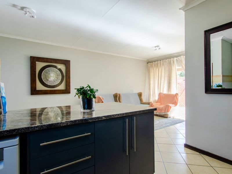Open plan living area featuring a modern kitchen island with granite countertops, dark cabinetry, and neutral ceramic floor tiles leading to a bright living space.