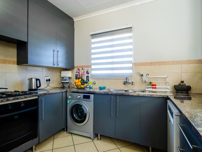 A functional kitchen featuring modern dark grey cabinetry, granite countertops, a built-in oven with gas hob, and integrated laundry plumbing.