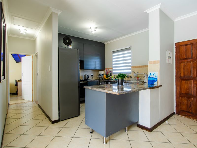 A functional kitchen featuring dark cabinetry, granite countertops, a breakfast bar, and tiled flooring, with a convenient layout and neutral wall finishes.