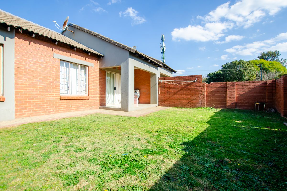 A private rear garden featuring a brick boundary wall, a covered patio area, and a lawn, providing a functional outdoor space for the townhouse.