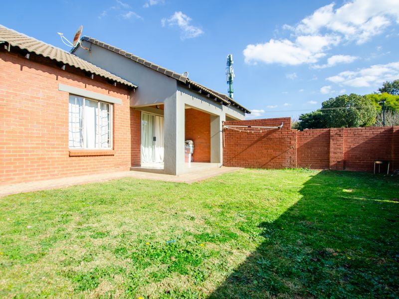 A private rear garden featuring a brick boundary wall, a covered patio area, and a lawn, providing a functional outdoor space for the townhouse.