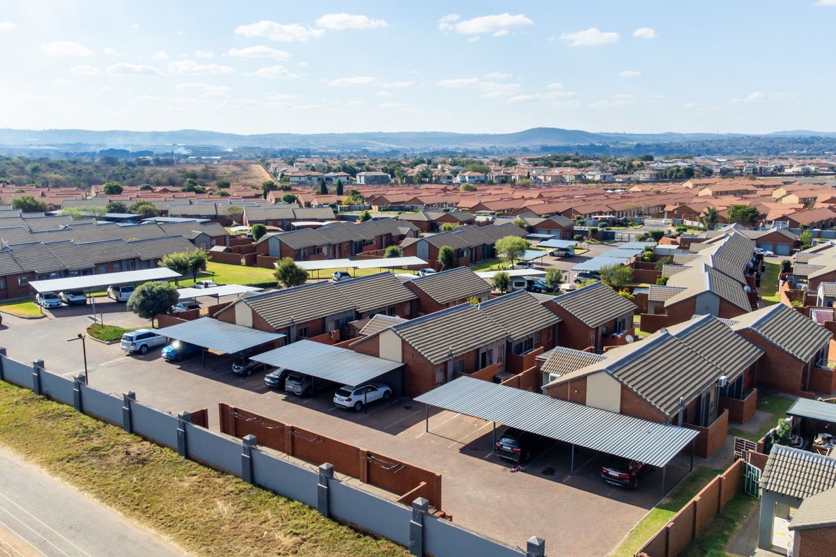 Aerial view of a residential townhouse complex featuring multiple units with tiled roofs, covered carports, and paved driveways within a secure perimeter.