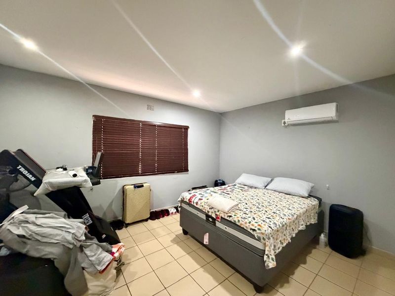 A spacious bedroom featuring tiled flooring, recessed ceiling lighting, and a wall-mounted air conditioning unit.