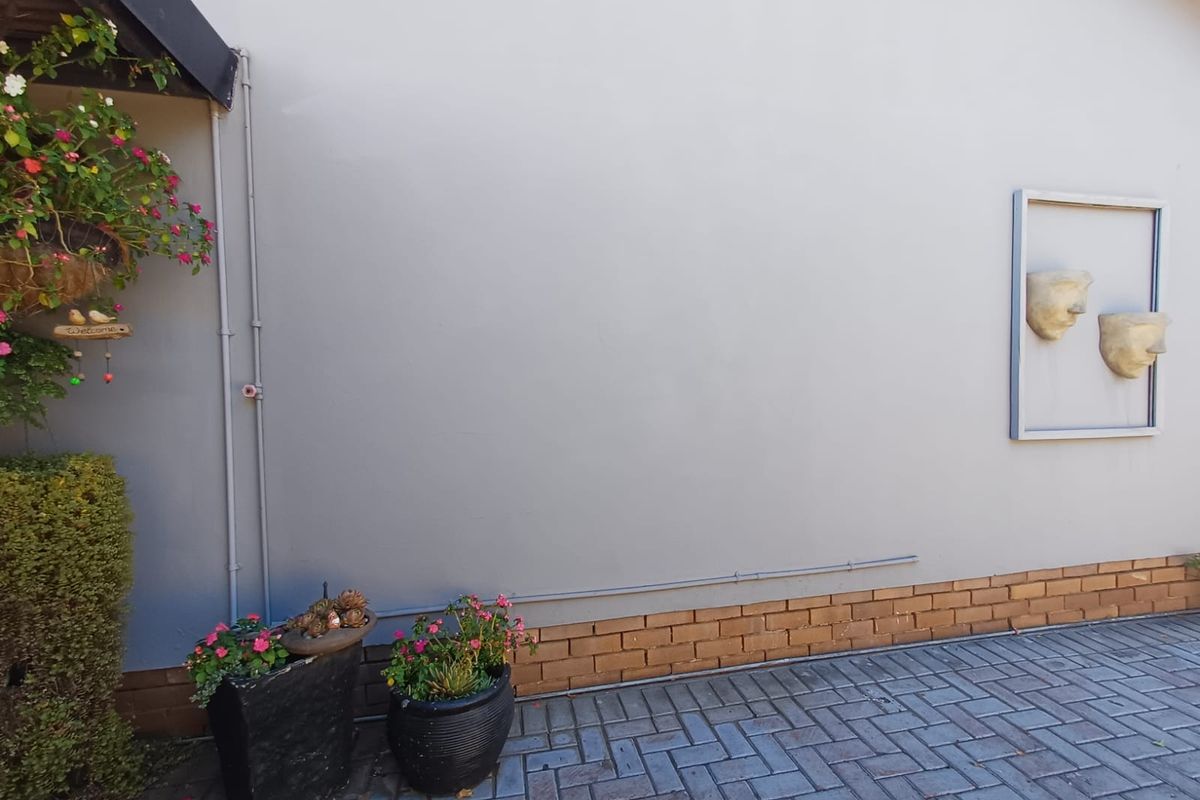 A view of a side exterior wall featuring a brick base, smooth rendered finish, and paved ground surface.