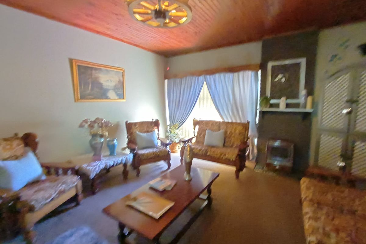 A traditional living room featuring a brick fireplace, timber-clad ceiling, and carpeted flooring, offering a cozy, dated aesthetic.