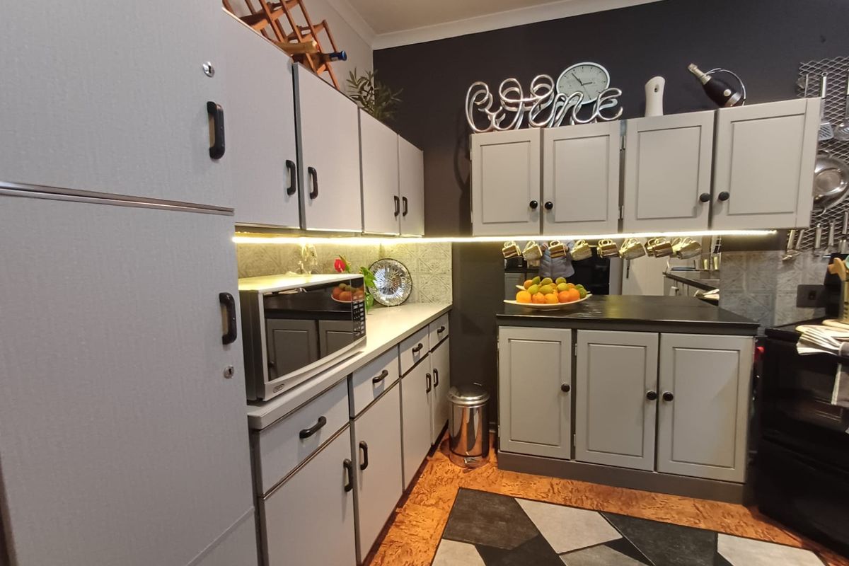 A compact kitchen featuring light grey cabinetry, dark countertops, under-cabinet LED lighting, and a unique geometric patterned floor.