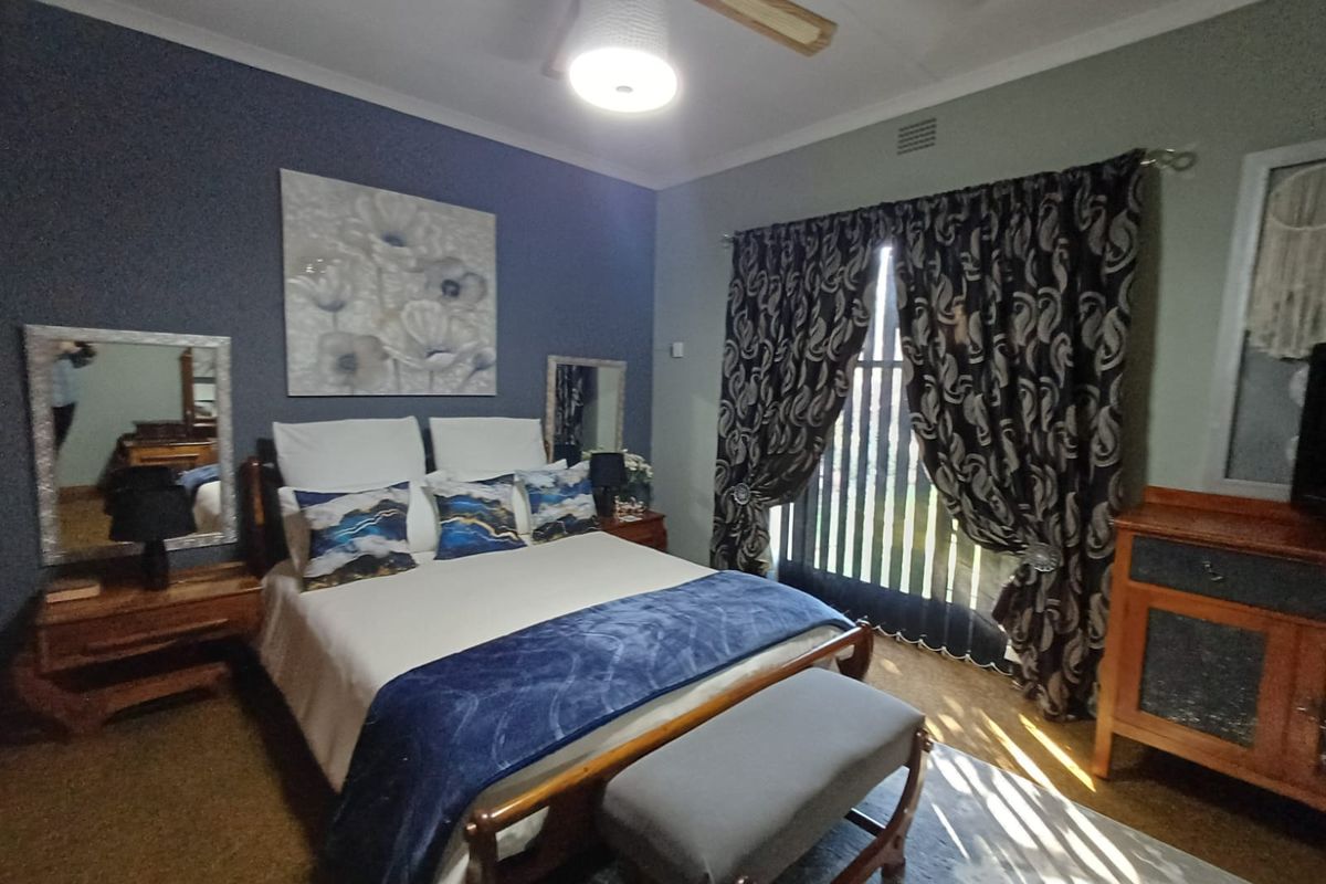 A well-lit bedroom featuring a ceiling fan, vertical blinds, and a dark accent wall, providing a comfortable and functional sleeping space.