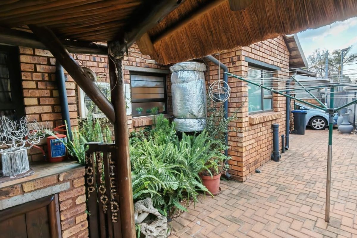 A rear exterior view featuring a brick-paved patio area, exposed brick walls, a thatched roof overhang, and a wall-mounted geyser.
