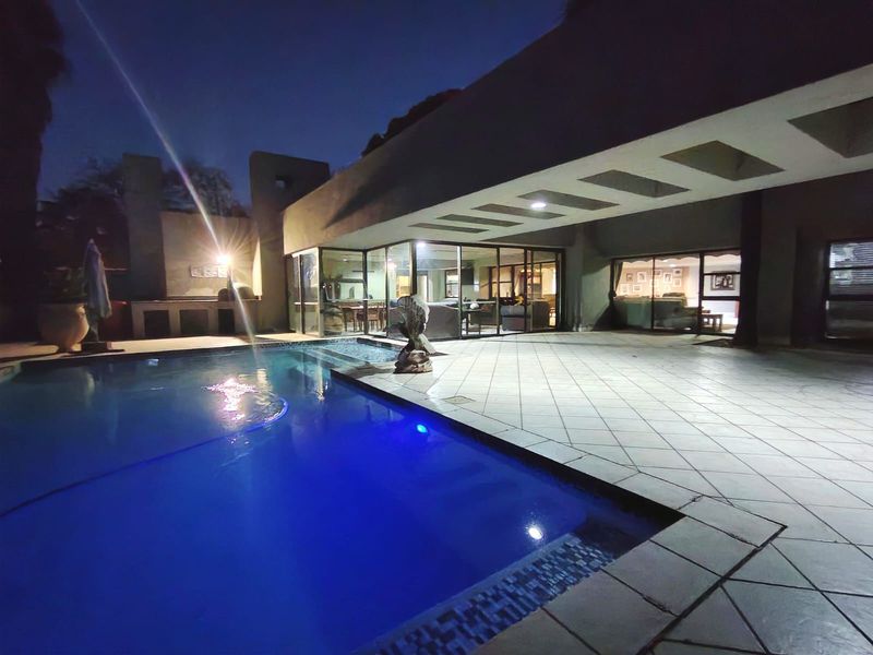Night view of a swimming pool and spacious covered patio area with built-in braai, featuring direct access to the interior living spaces.