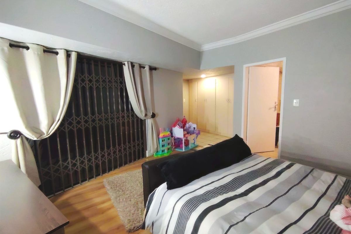 Spacious bedroom featuring laminate flooring, built-in cupboards, and a sliding door with a security gate leading to an outdoor area.