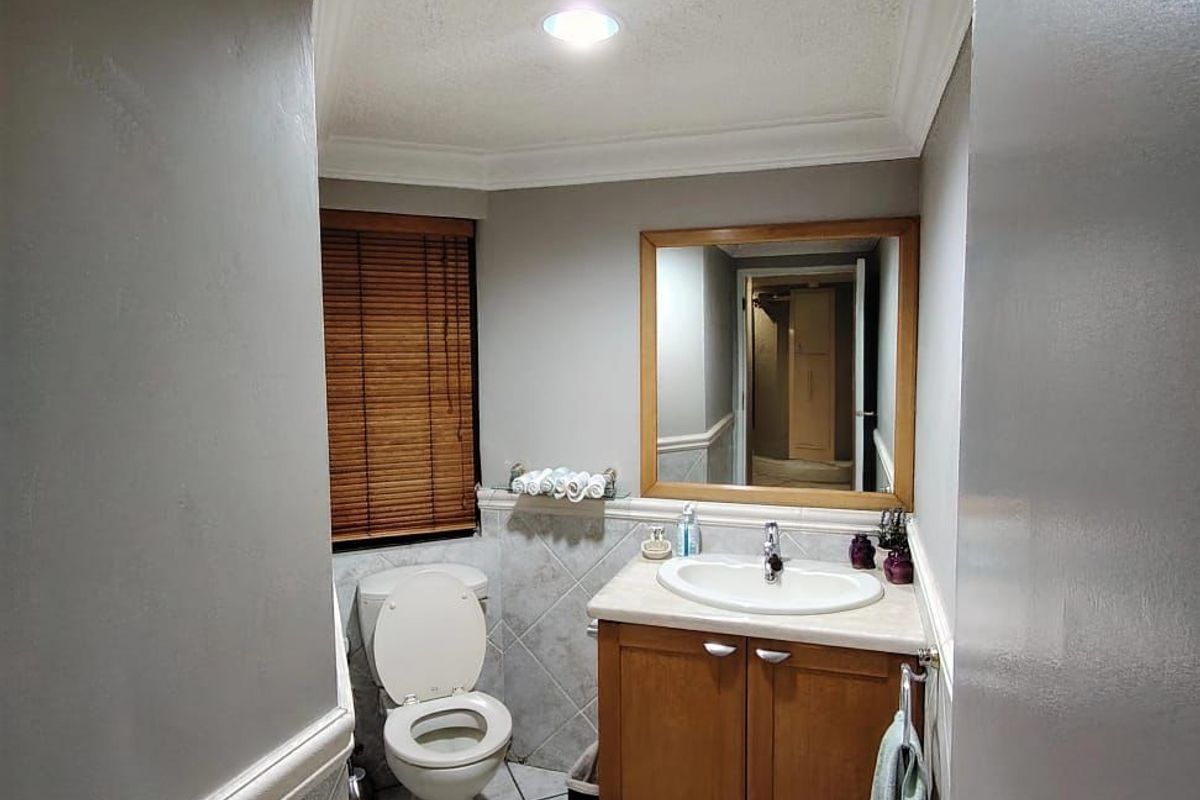 A compact bathroom featuring a wooden vanity, ceramic sink, toilet, tiled flooring, and wall tiling with crown molding detail.