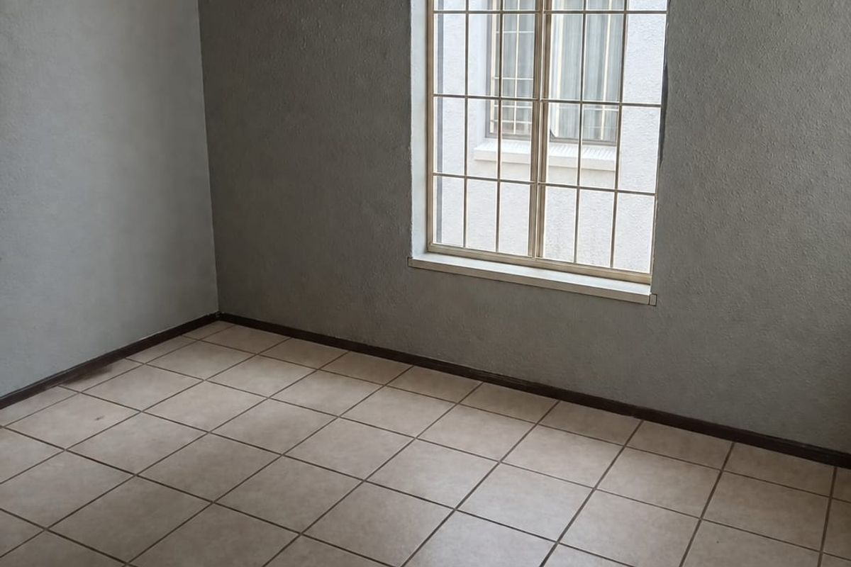 A vacant bedroom featuring neutral tiled flooring, grey painted walls, and a window fitted with security burglar bars.