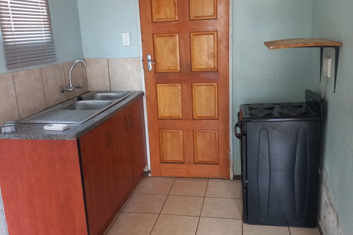 A compact kitchen featuring a double sink, built-in cabinetry, and a freestanding stove, with tiled flooring and a wooden door.