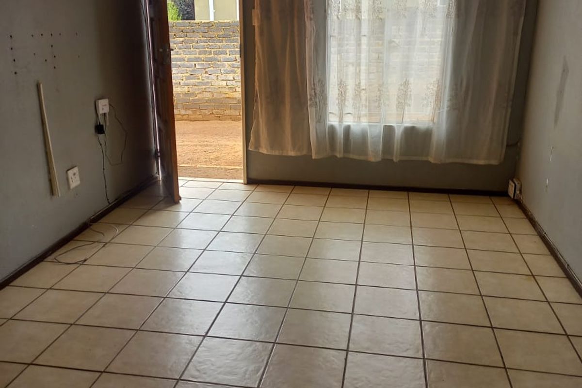An empty living room featuring tiled flooring, a central light fixture, and direct access to the rear exterior area.