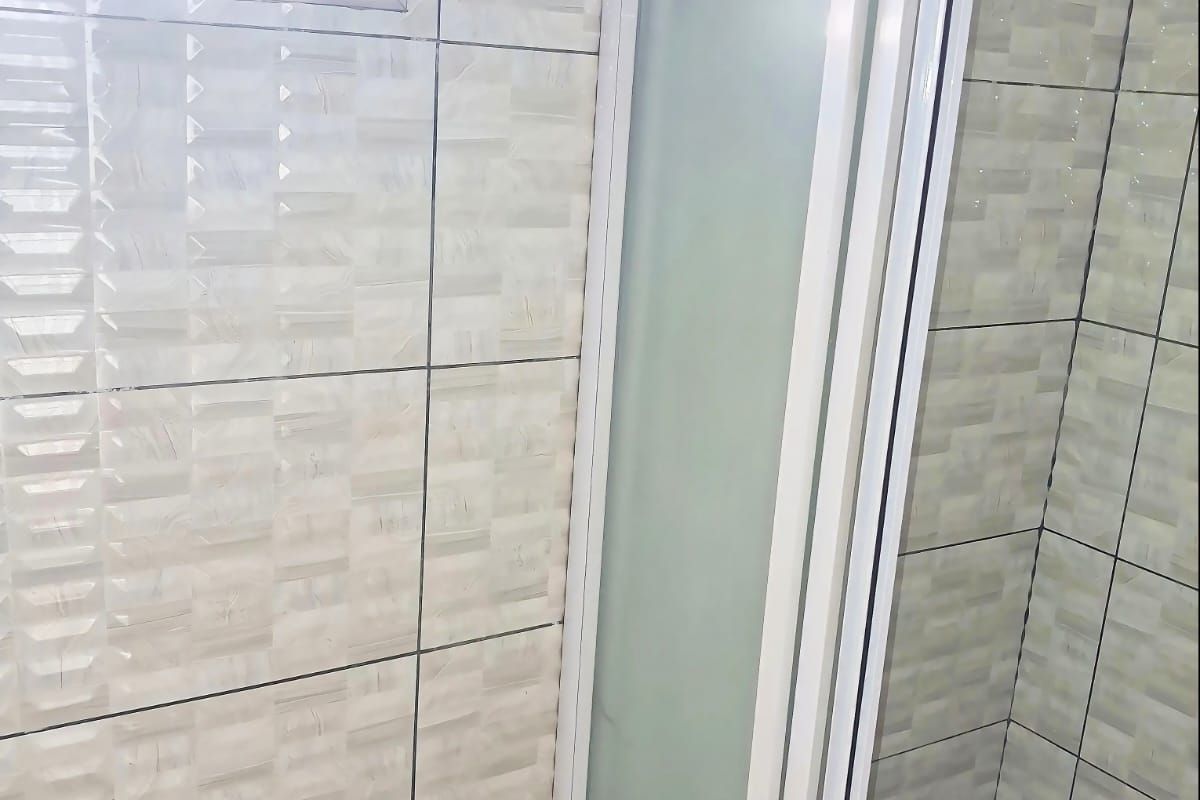 A bathroom shower enclosure featuring textured wall tiles, a frosted glass door, and a small window with fitted blinds.