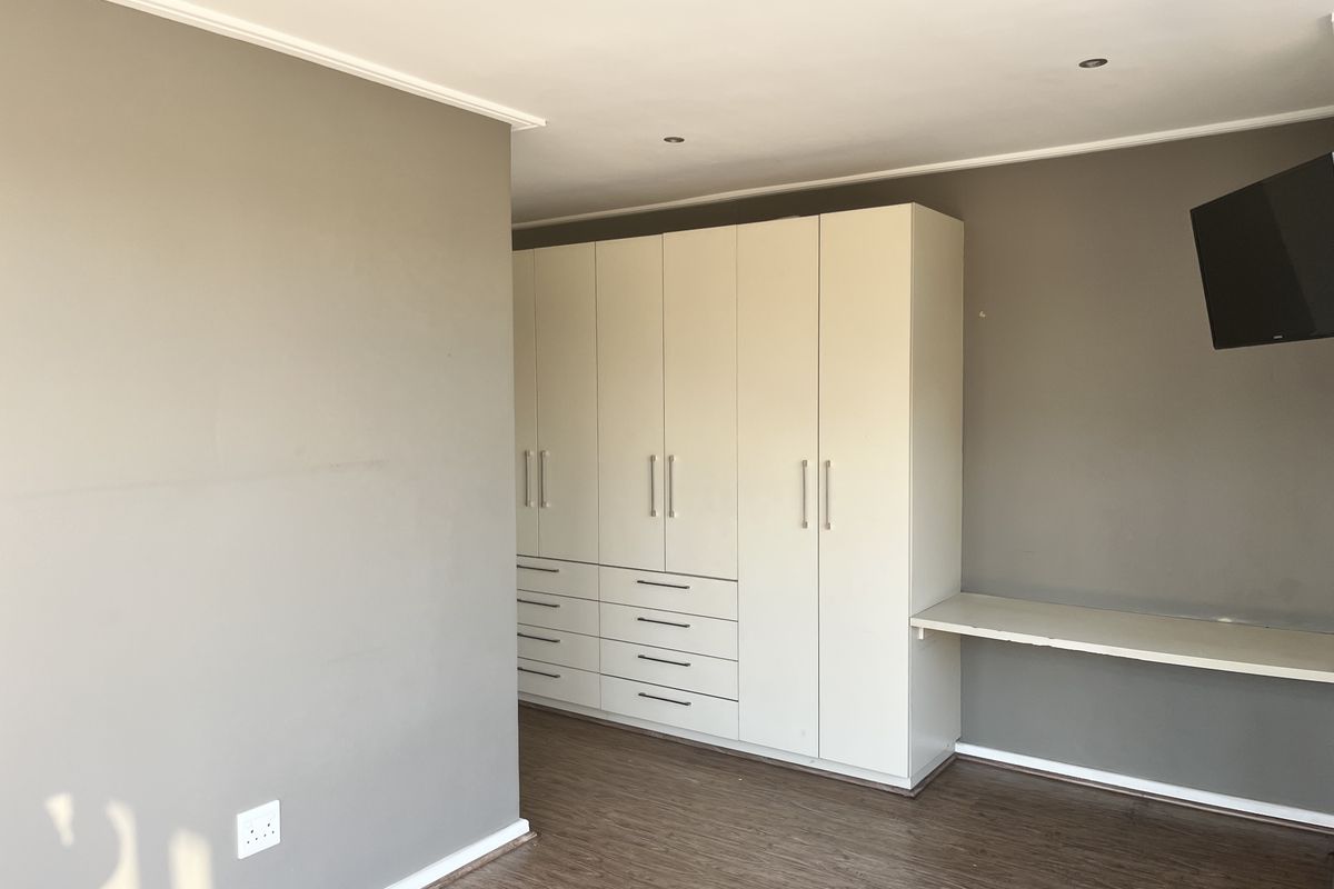 A bedroom featuring built-in cabinetry with integrated drawers and a desk surface, finished with wood-look flooring and neutral wall tones.