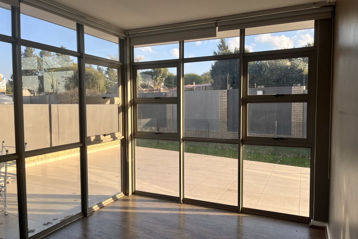 Bright living area featuring floor-to-ceiling aluminium-framed windows with direct access to an outdoor tiled patio and garden area.
