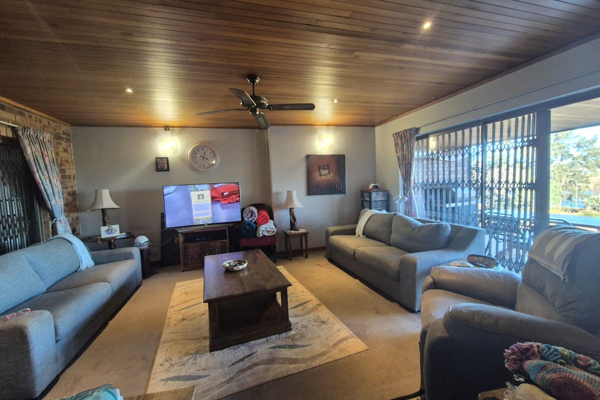 A spacious living room featuring a distinctive timber-paneled ceiling, recessed lighting, and large sliding glass doors with security gates leading to the outdoors.