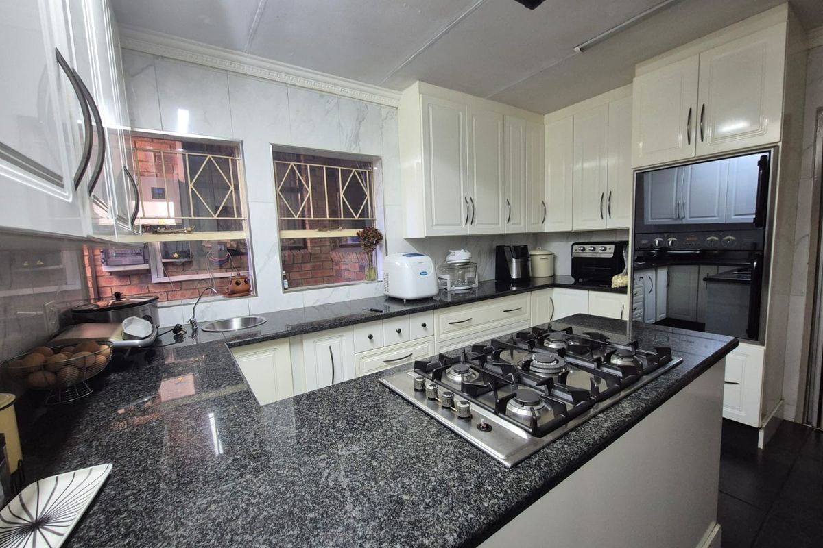 A functional kitchen featuring granite countertops, built-in gas hob, integrated oven, and ample white cabinetry with marble-look wall tiling.