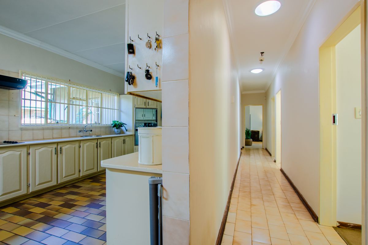 A view from a tiled hallway looking into a kitchen featuring traditional cabinetry, a built-in oven, and a window with security bars.