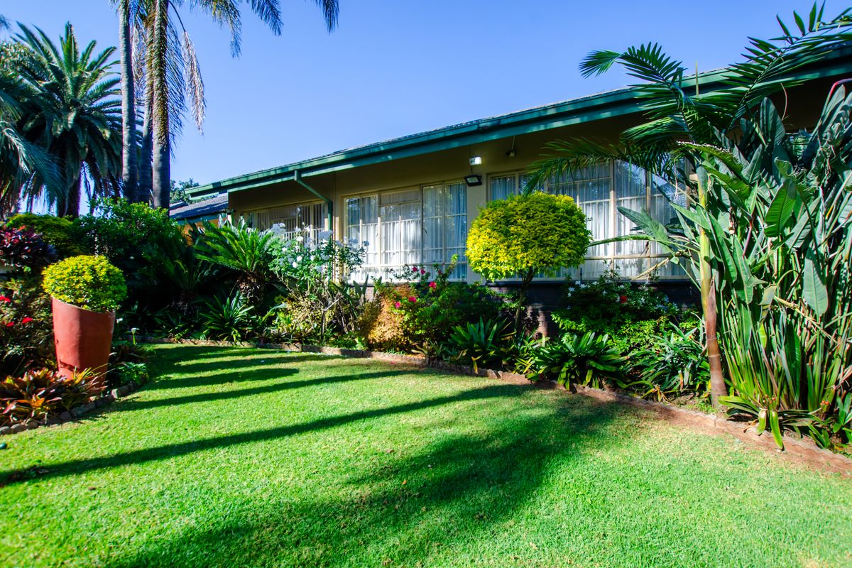 A well-maintained rear garden featuring a lush green lawn, mature landscaping, and a view of the home's rear exterior facade with large windows.