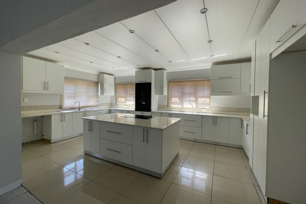 Spacious modern kitchen featuring a central island, white cabinetry, stone countertops, and tiled flooring. The area is bright and ready for final finishing touches.