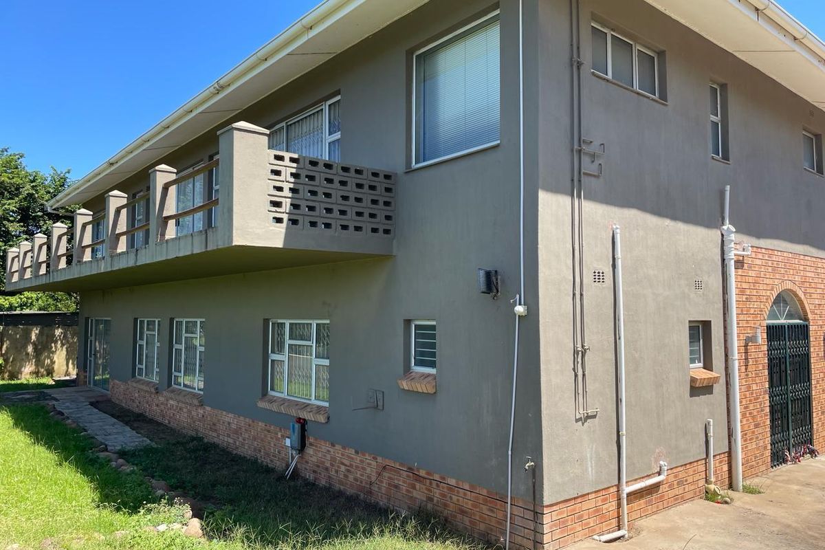 Rear exterior view of a two-story house featuring a balcony, brick and plaster facade, and security window bars.