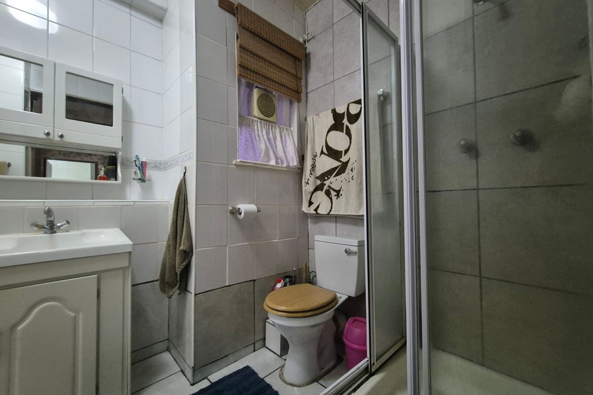 A functional bathroom featuring a vanity with integrated basin, a toilet, and a glass-enclosed shower cubicle with tiled walls.