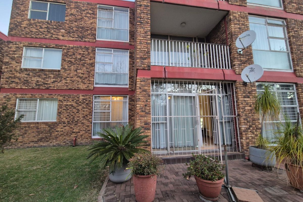 Rear view of a multi-story flat complex featuring face-brick facade, private balconies with metal railings, and ground-level paved patio area.
