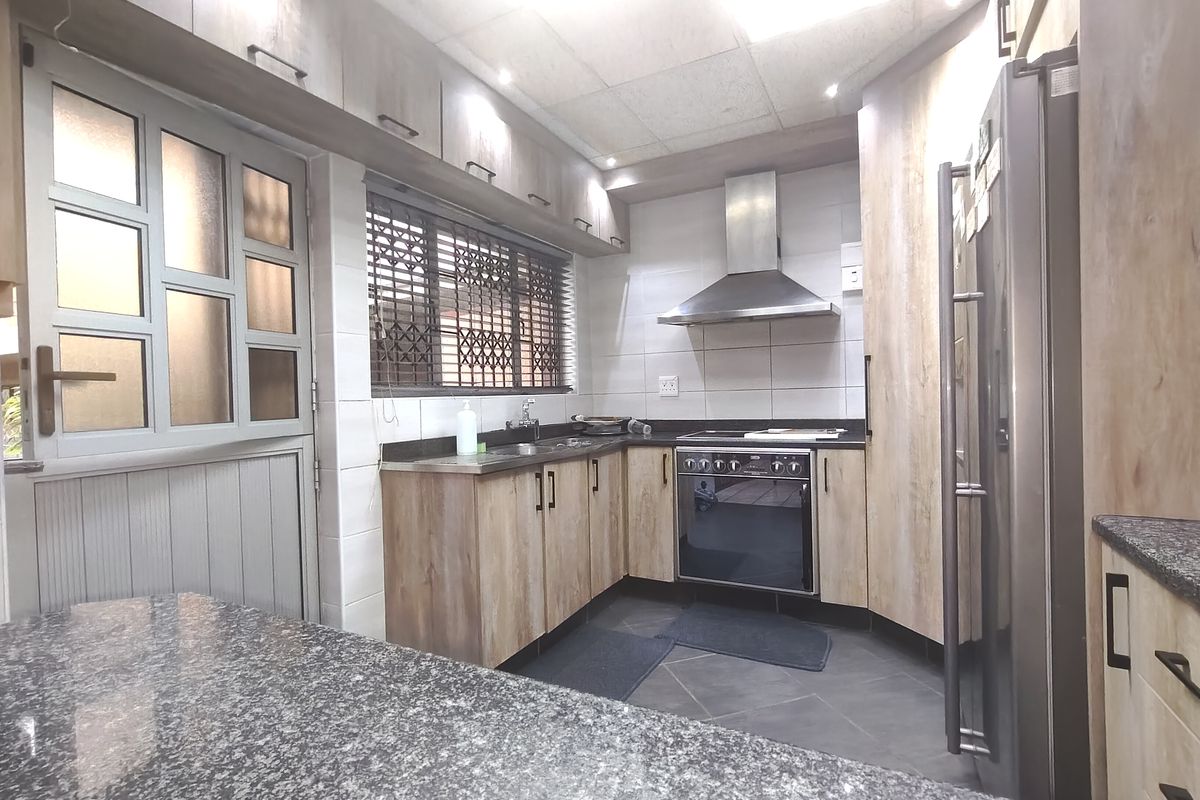 A functional kitchen featuring wood-look cabinetry, granite countertops, a built-in oven with extractor fan, and a tiled backsplash.