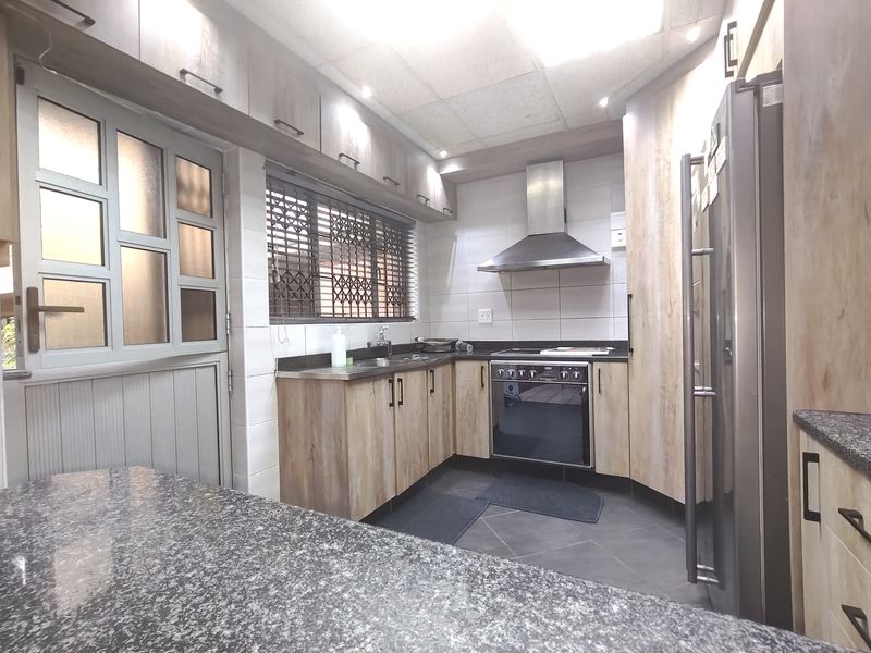 A functional kitchen featuring wood-look cabinetry, granite countertops, a built-in oven with extractor fan, and a tiled backsplash.