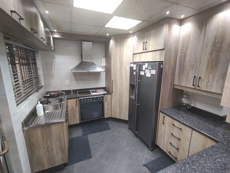 A functional kitchen featuring wood-look cabinetry, granite countertops, stainless steel appliances, and tiled flooring with integrated lighting.
