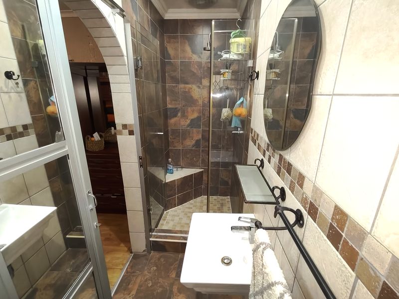 A compact bathroom featuring a walk-in shower with tiled walls, a wall-mounted basin, and decorative tile accents throughout the space.