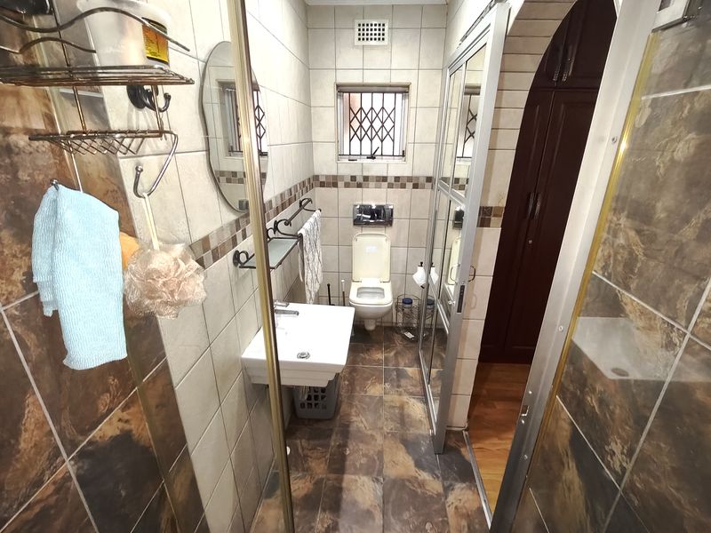 A functional bathroom featuring a wall-mounted basin, toilet, and a shower enclosure with tiled walls and flooring.