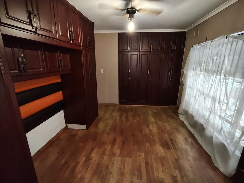 Spacious bedroom featuring extensive dark wood built-in cabinetry, parquet flooring, and a ceiling fan, offering a functional layout ready for modern updates.