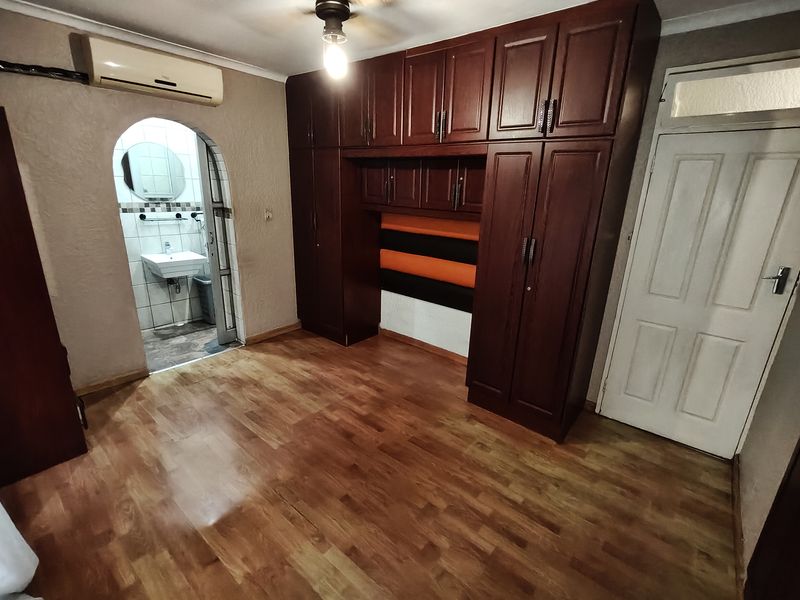 Bedroom featuring extensive built-in wooden cabinetry, laminate flooring, and an arched doorway leading to an en-suite bathroom.