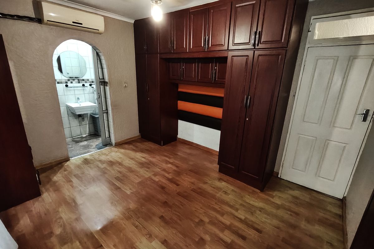 Bedroom featuring extensive built-in wooden cabinetry, laminate flooring, and an arched doorway leading to an en-suite bathroom.