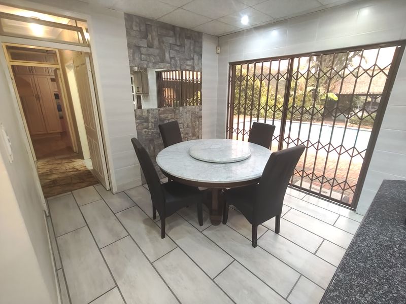 Dining area featuring tiled flooring, decorative stone wall accents, and a sliding glass door with security gate leading to the outdoor pool area.
