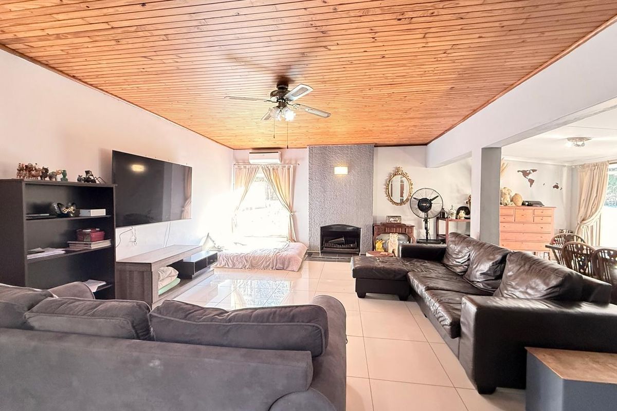 Spacious living room featuring a timber-clad ceiling, tiled flooring, and a built-in fireplace, offering a comfortable and functional family living space.