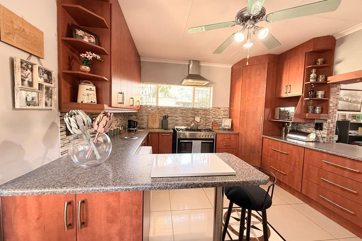 A functional kitchen featuring warm-toned built-in cabinetry, a gas stove with extractor fan, tiled backsplash, and a breakfast bar counter.