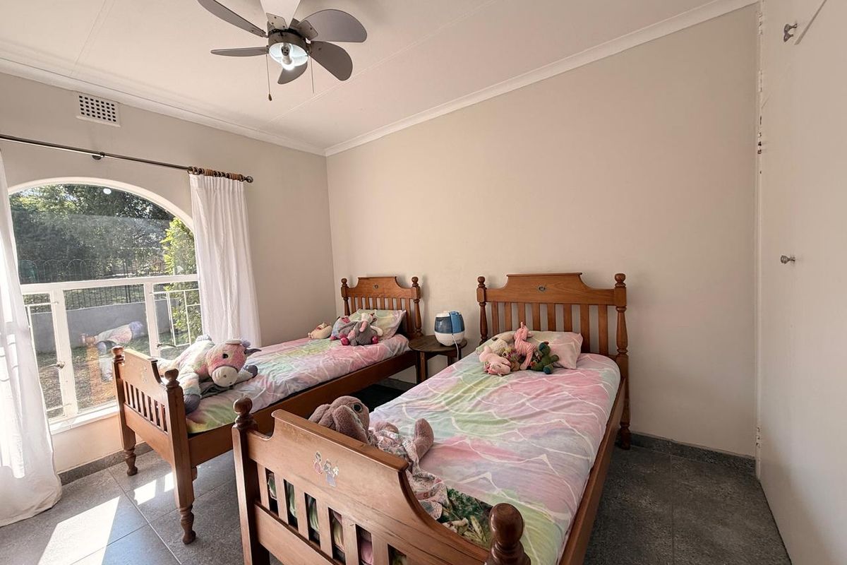 A bedroom featuring tiled flooring, an arched window providing natural light, and a ceiling fan.