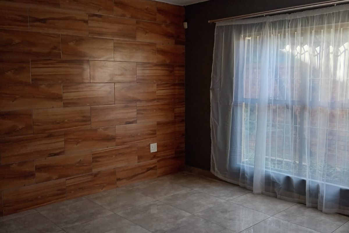 An empty living room featuring a wood-look tile accent wall, neutral ceramic floor tiles, and a large window with security bars.
