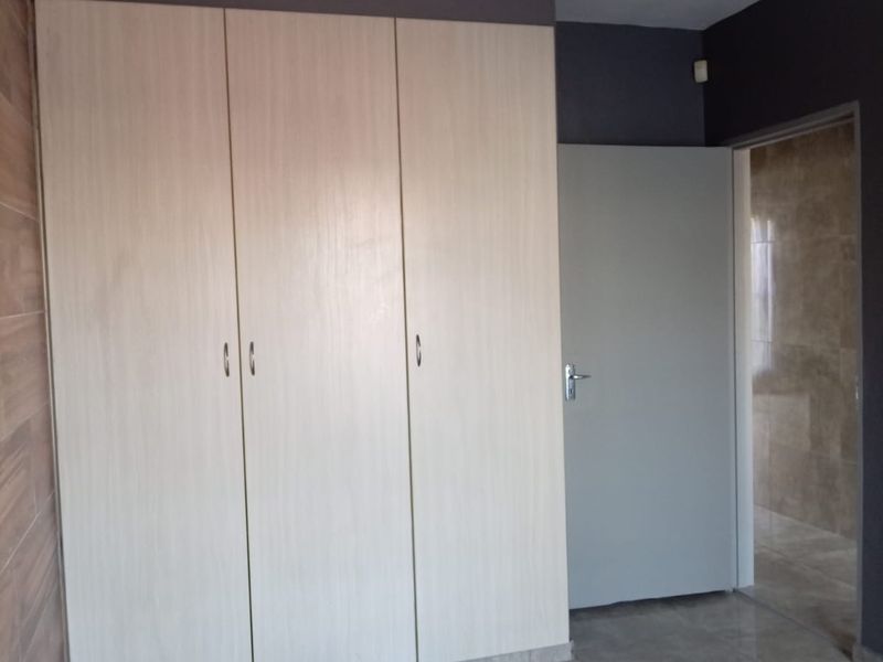 A clean, empty bedroom featuring light wood-finish built-in wardrobes, modern grey floor tiles, and a neutral color scheme.