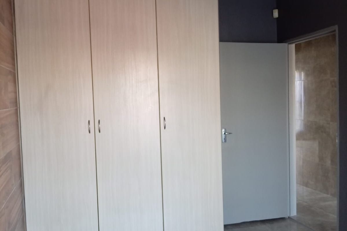A clean, empty bedroom featuring light wood-finish built-in wardrobes, modern grey floor tiles, and a neutral color scheme.