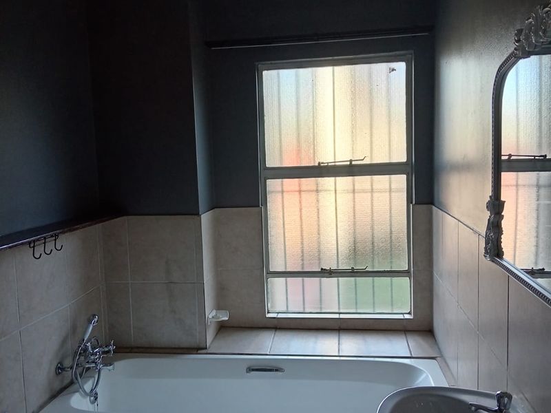 A functional bathroom featuring a bathtub, pedestal basin, and tiled splashbacks, illuminated by a large obscured glass window.