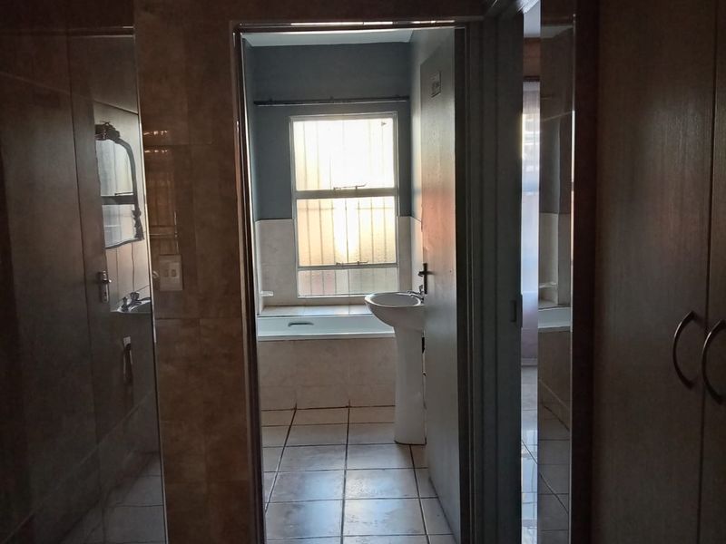 A view through a hallway into a bathroom featuring a pedestal basin, built-in bathtub, and tiled finishes.